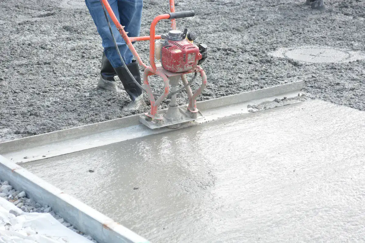 Power screed levelling a fresh concrete slab poured over a compacted stone base