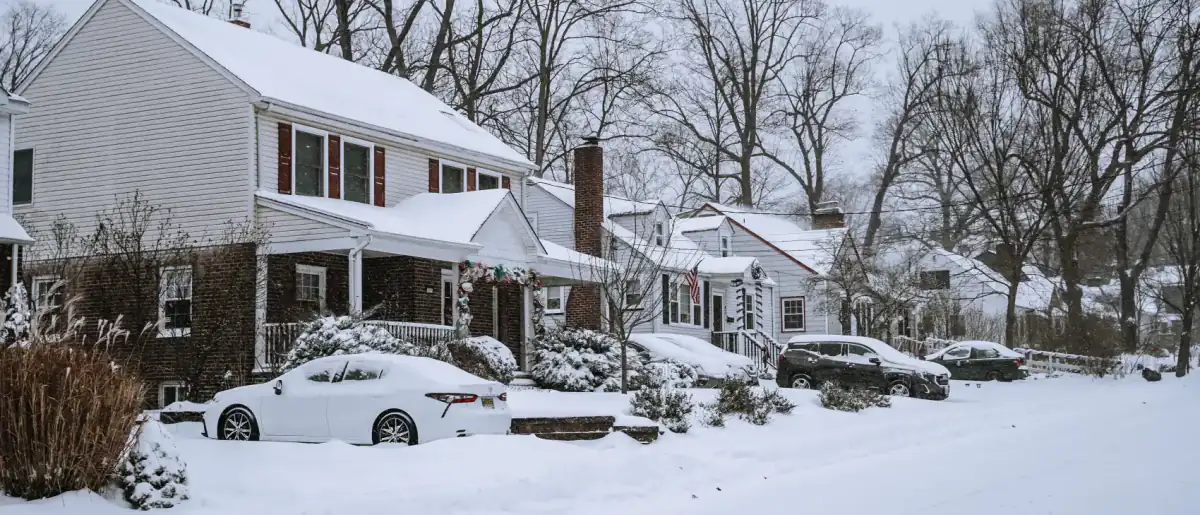 Snow-covered residential street lined with older houses and bare trees in winter
