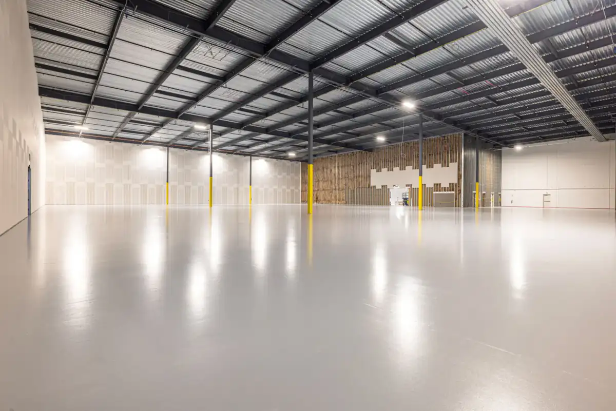 The interior of an empty warehouse with a large, flat, uninterrupted concrete floor running away to the far wall under steel roof framing.