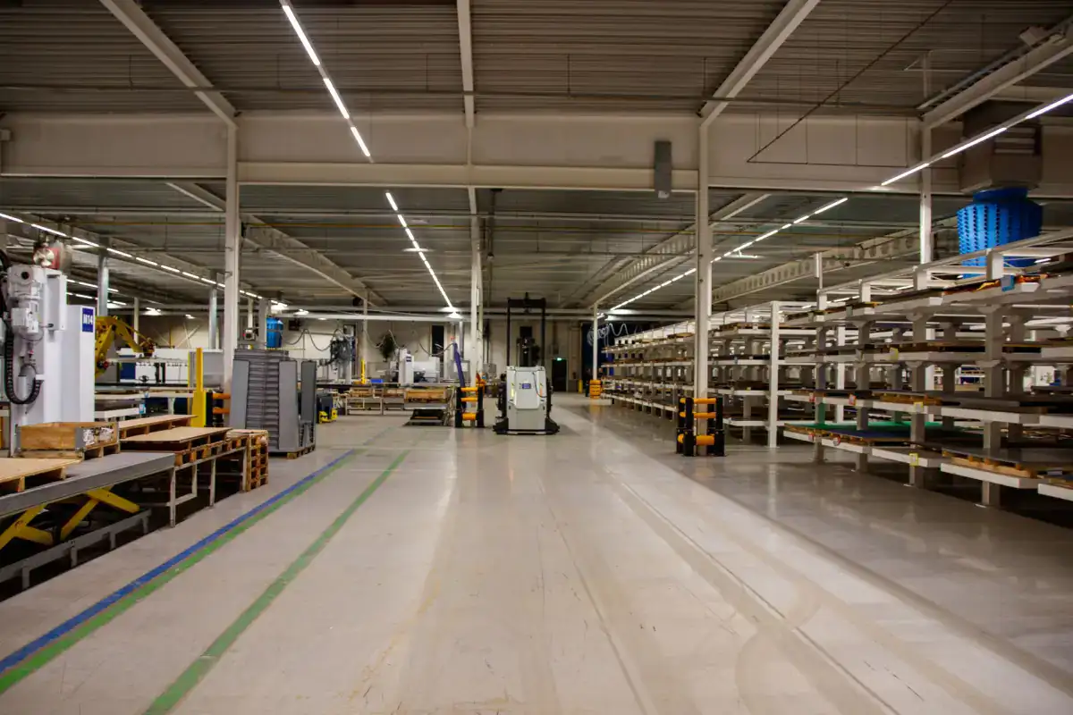 An industrial building interior with racking down one side and a pale concrete floor marked with painted aisle lines.
