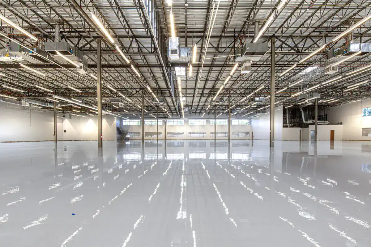 A large industrial floor slab reflecting rows of ceiling lights, with the saw-cut joint layout running across the surface.