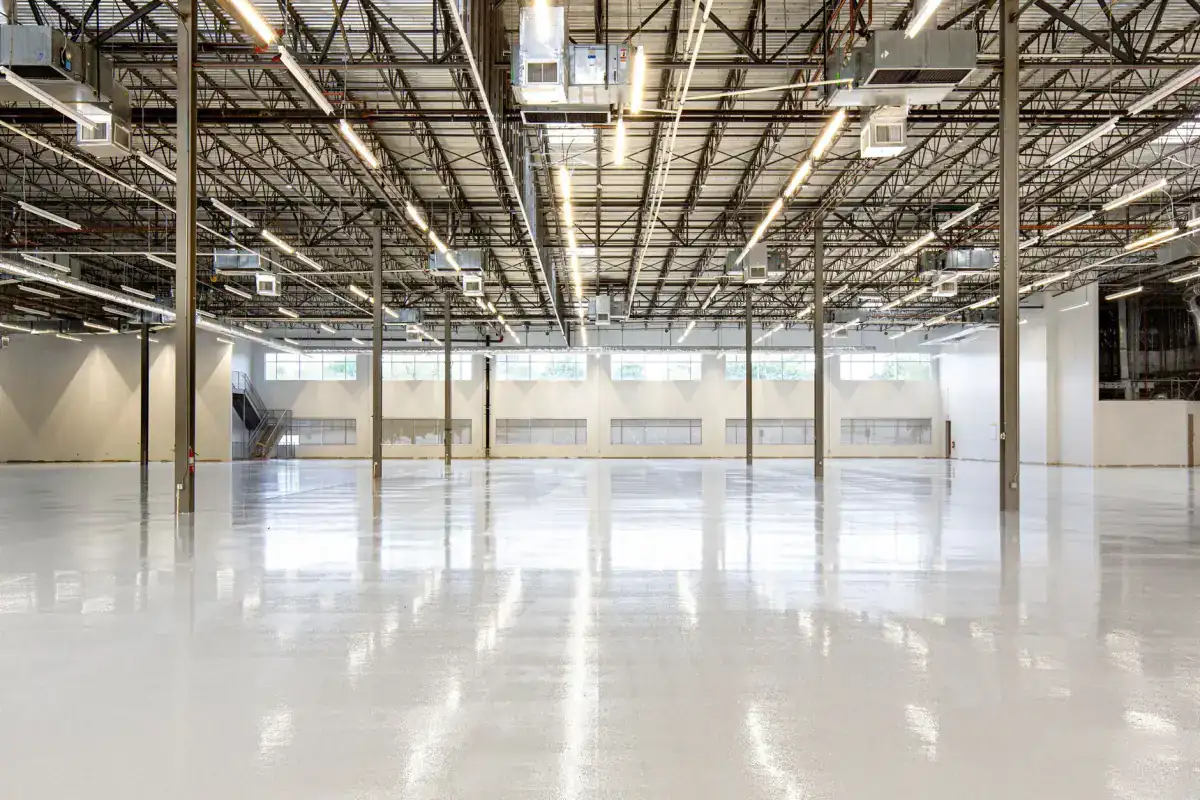A wide empty warehouse floor reflecting the overhead lighting in long unbroken lines, showing how flatness reads across a large slab.