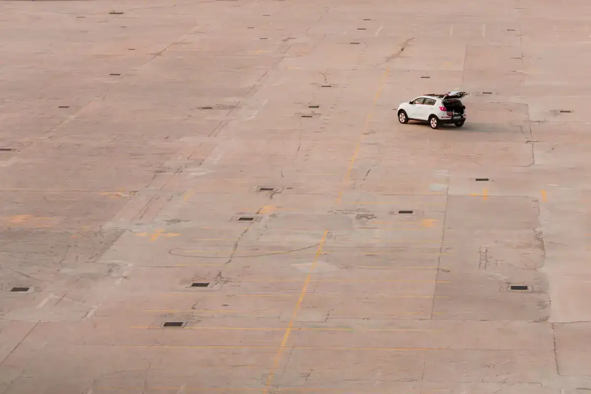 A large concrete paved area with the panel joint pattern running across it in a regular grid, a single car parked near the middle.