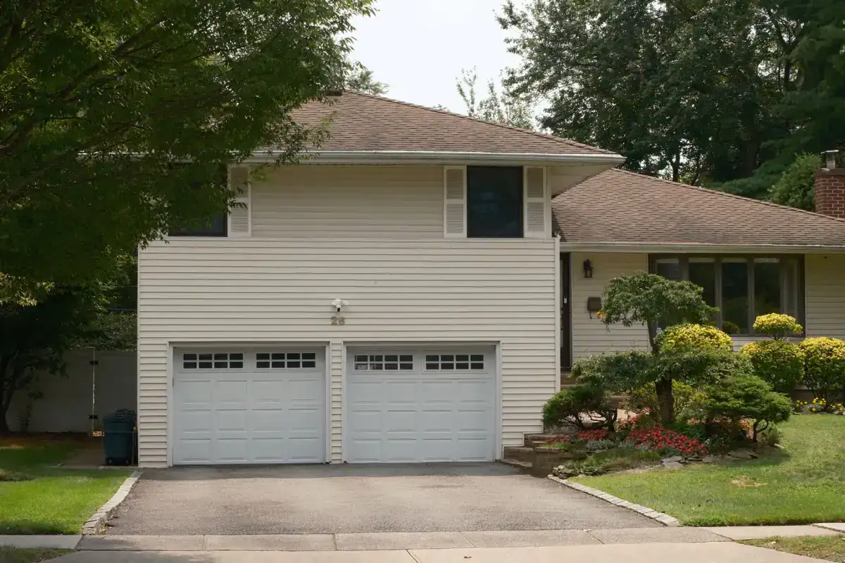 A concrete driveway serving a two-car garage on a mature lot, with the drive widening toward the garage doors and meeting the public sidewalk at the street.
