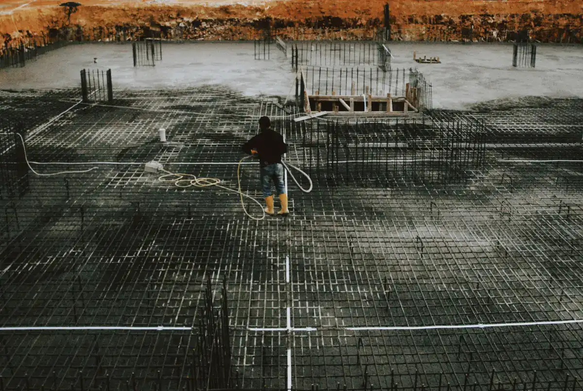 A worker moving a hose across a reinforced foundation area, with the tied bar grid and formed edges laid out over the prepared bearing surface.