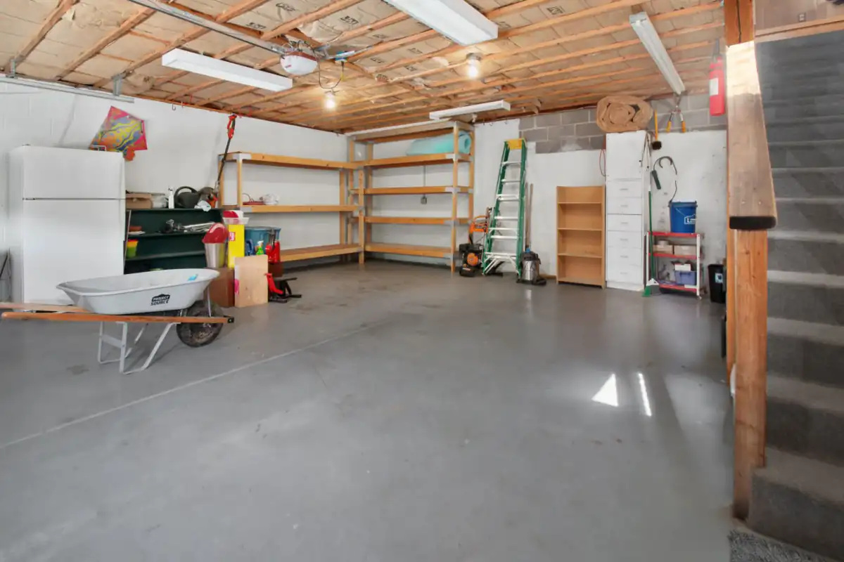 The interior of a residential garage with a clean, level concrete floor, shelving and a workbench along the walls and a wheelbarrow standing to one side.