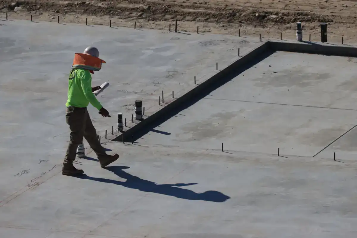 A poured concrete slab with a formed perimeter edge and anchor bolts set into the surface, the arrangement used where a garage wall lands on the slab.