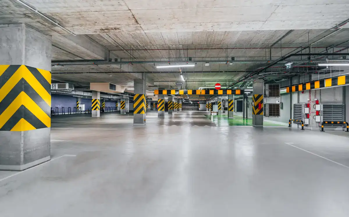 A large concrete parking floor inside a structure, with heavy columns marked in hazard striping and a smooth, hard-wearing slab surface running between them.