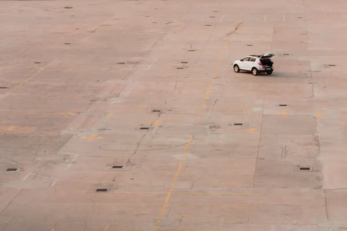 A large concrete parking area with its panel joints laid out in a regular grid across the surface and a single car parked toward the middle.