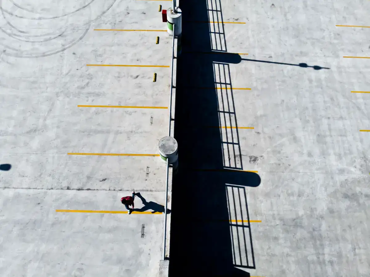 An overhead view of a concrete parking deck with yellow bay striping painted across the slab and a pedestrian crossing it.