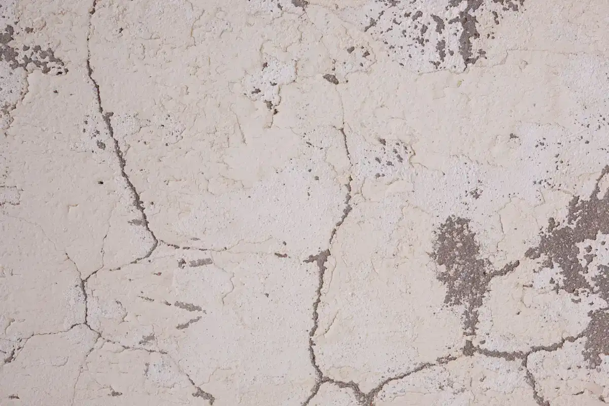 A network of fine cracks spreading across a pale concrete surface, the shallow crazing pattern that sits in the top layer rather than through the slab.
