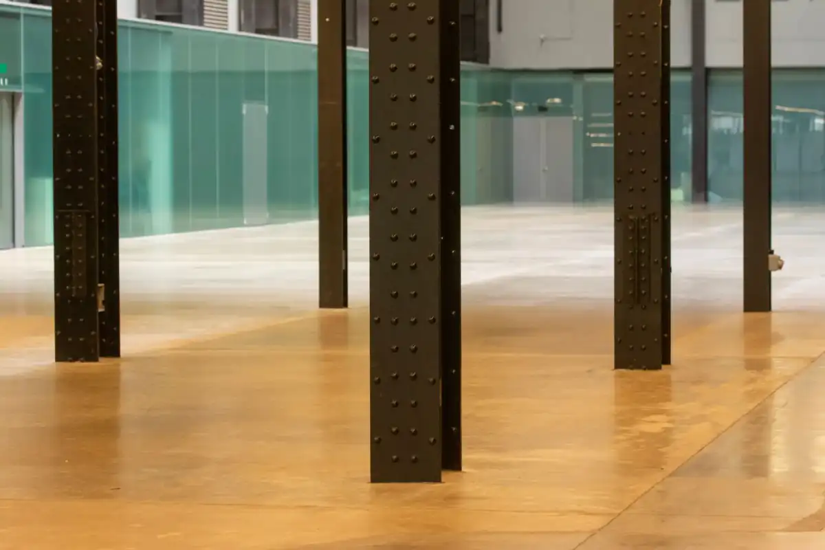 A smooth, warm-toned polished concrete floor running between steel columns in an open interior, the kind of restored surface an overlay is meant to deliver.