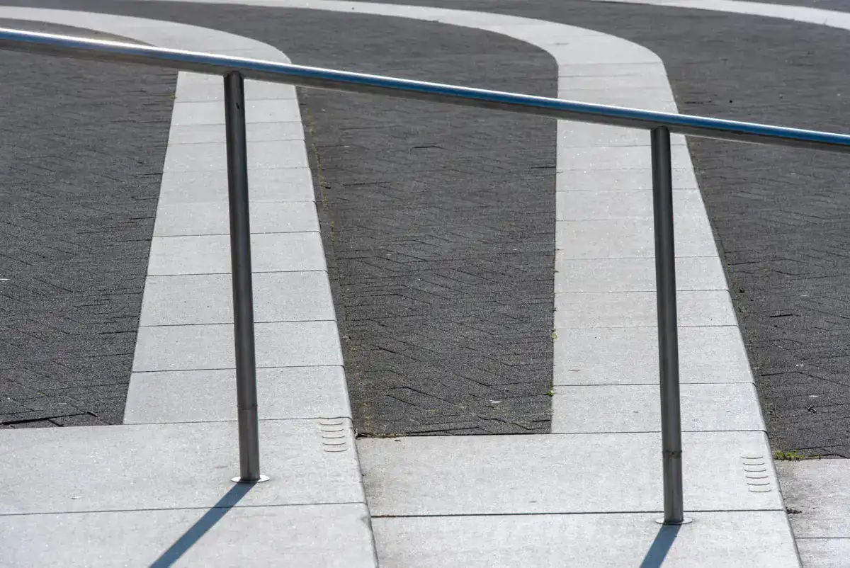 A concrete walkway rising alongside metal handrails, with the ramped section and the level landing meeting in clean panels of pale concrete.