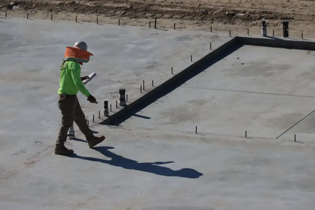 A large finished concrete slab with anchor bolts standing proud of the surface along a formed edge, ready for a structure to be set on it.