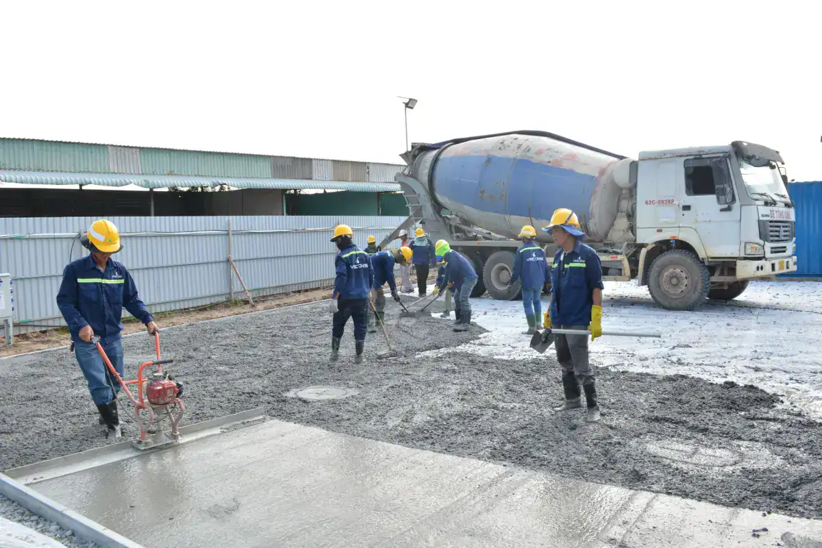 A crew in hard hats placing and levelling concrete for a slab while a ready-mix truck stands alongside the pour.