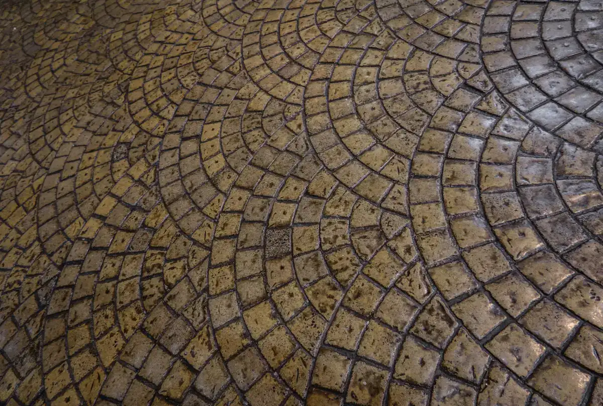 A stamped concrete surface laid out in a radial cobblestone fan pattern, with the individual stone impressions and their joint lines curving across the slab.